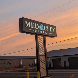Med City Dental clinic sign illuminated at sunset, with a modern industrial building in the background